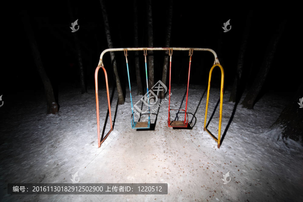 古老的生銹的秋千站在黑暗的公園冬天的夜晚；地上的白雪
