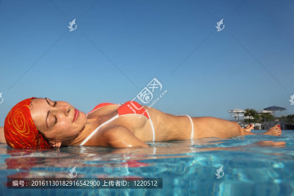 在紅色的泳衣在水中游泳池曬日光浴的年輕漂亮的女人；從水下包