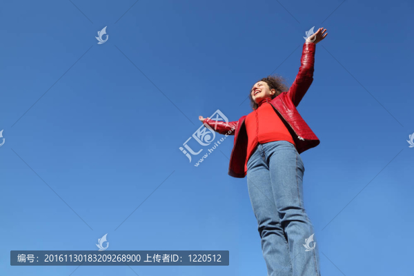 美麗的年輕女子穿著紅夾克和藍(lán)色牛仔褲向天空舉起雙手