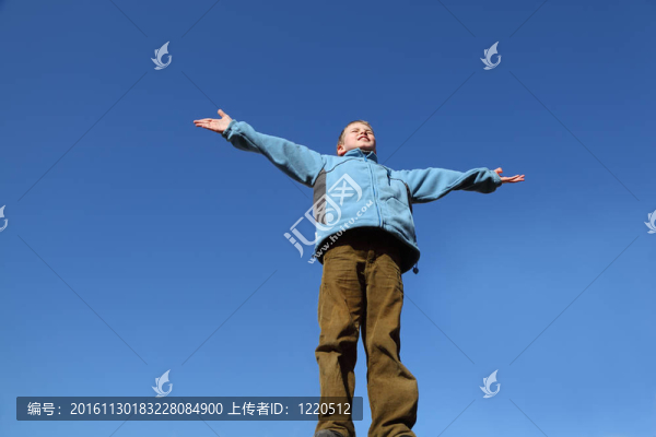 穿著藍色夾克和棕色褲子的小男孩舉起雙臂向藍天