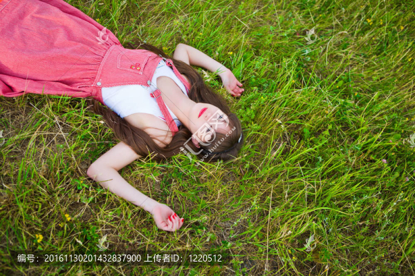 紅色的無(wú)袖短上衣的漂亮女孩躺在綠色的草地上