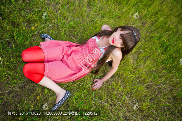 紅色的無袖短上衣的漂亮女孩躺在綠色的草地上