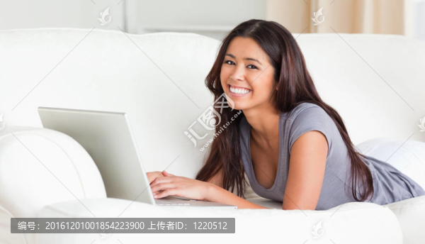 可愛(ài)的女人躺在沙發(fā)上用筆記本看著相機(jī)