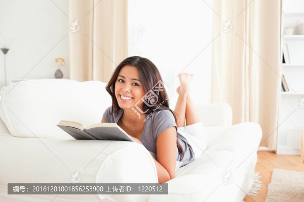 微笑的女人躺在沙發(fā)上看書
