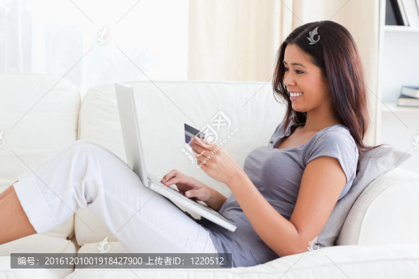 微笑的女人坐在沙發(fā)上拿著信用卡