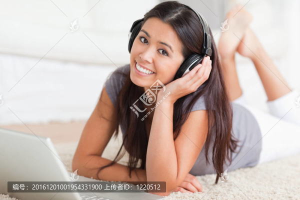 靠近一個(gè)可愛的女人躺在客廳的地毯在筆記本和耳機(jī)
