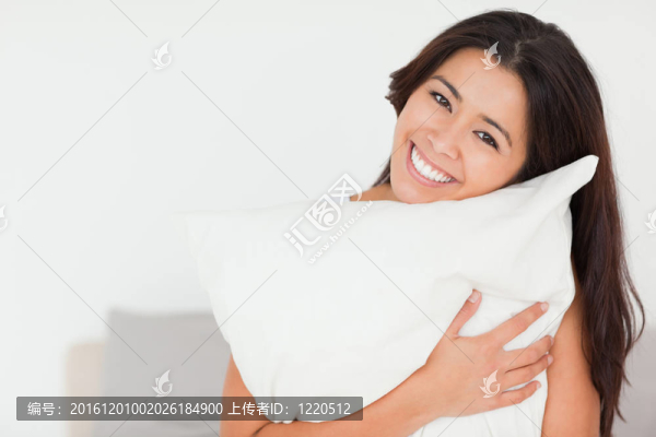 一個(gè)迷人的女人與枕頭坐在床上看著相機(jī)在臥室