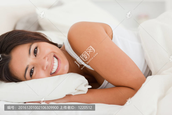 一個微笑可愛的女人躺在床單下