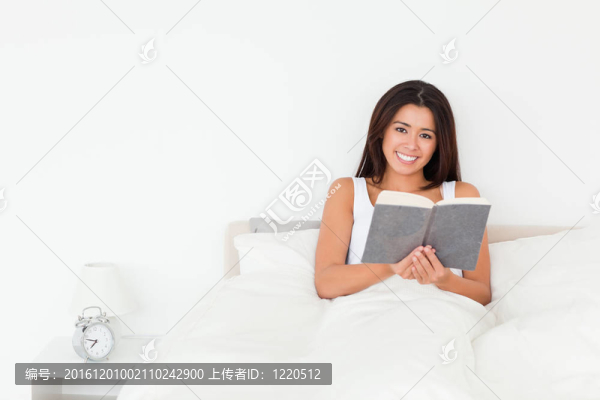 黑發(fā)女人抱著書在床上看著lyling相機(jī)在臥室