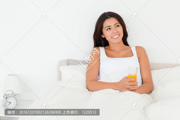黑發(fā)女子拿著橙汁坐在床上看著臥室的天花板