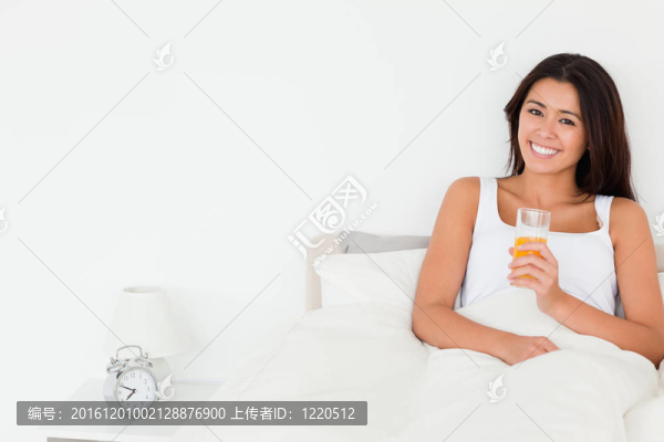 黑發(fā)女子喝橙汁坐在床上看著