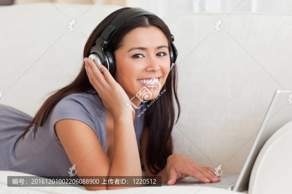 靠近一個躺在沙發(fā)看耳機的迷人的女人