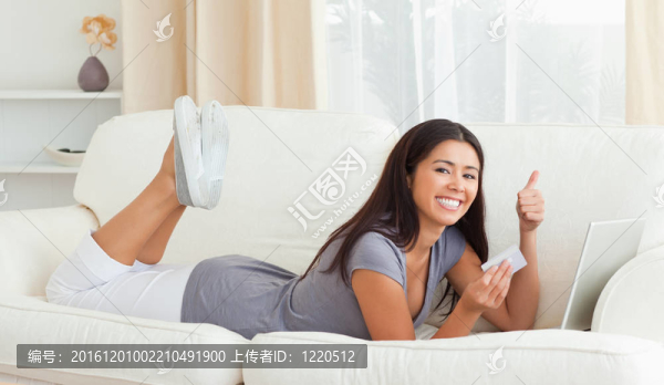 微笑的女人用大拇指和卡片在手躺在沙發(fā)上