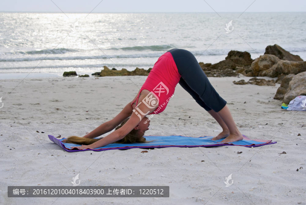 一個運動的棕色頭發(fā)的女人做瑜伽練習(xí)下犬式或下犬式姿勢在空曠的海灘在墨西哥日落時分在佛羅里達(dá)州那不勒斯