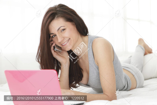 女孩在床上使用手機和電腦時微笑愉快