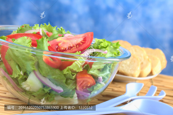 由西紅柿沙拉；生菜；紅甜椒；紅洋蔥和黃瓜放在一個玻璃碗在后面邊上的一個藍色塑料沙拉和面包片服務器（選