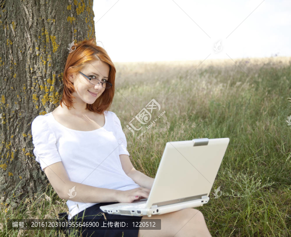 在白色的眼鏡和筆記本電腦坐在樹的年輕女性。