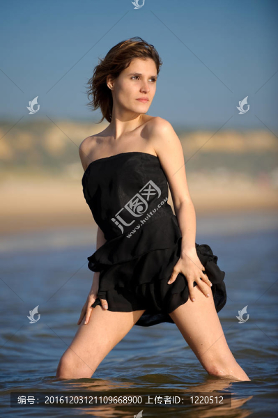 在海灘上穿著黑色連衣裙的年輕漂亮女人