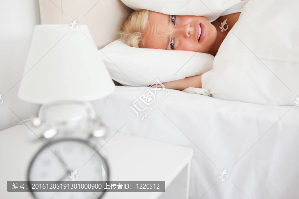 累了的女人隱藏她的頭在枕頭，鬧鐘在她的臥室里響起