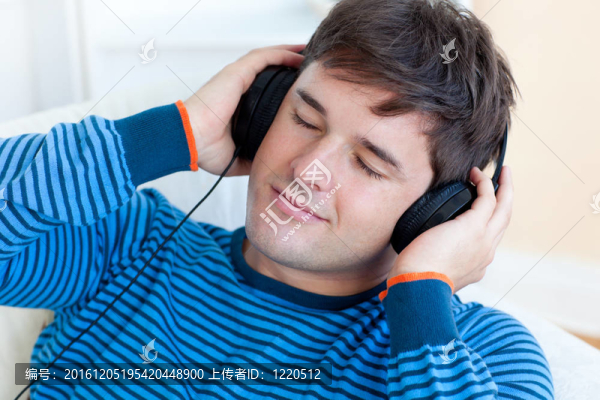 和平的人聽(tīng)音樂(lè)抱著他的earphoneslying在客廳沙發(fā)上