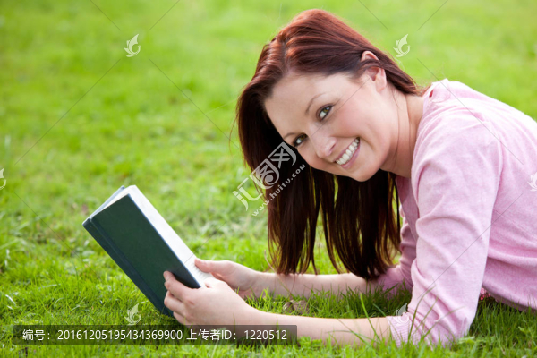 可愛的女人躺在草地上看書