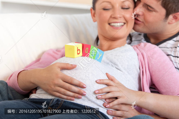 年輕人親吻他懷孕的妻子，用嬰兒的字母在肚子上躺在家里的沙發(fā)上