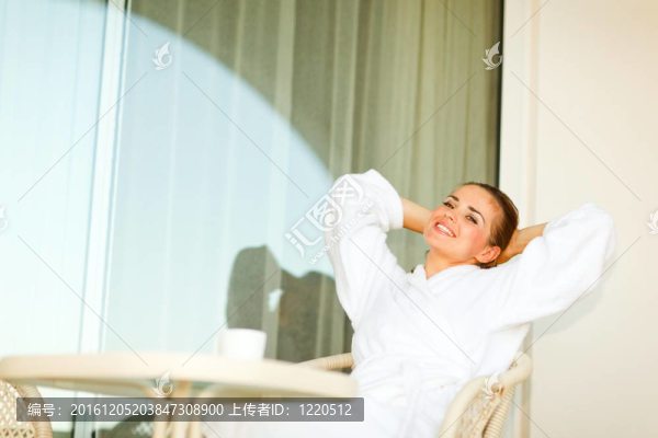 在浴袍坐在桌邊上的年輕女子和放松的陽臺(tái)