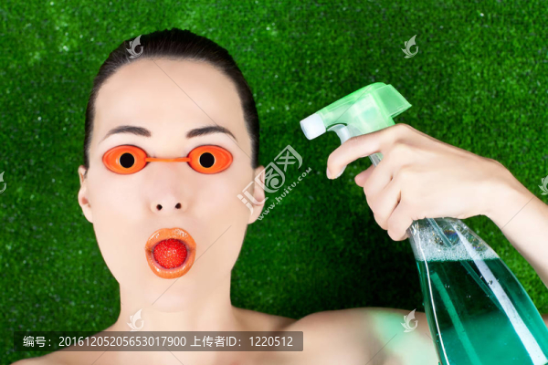 特寫鏡頭的一個美麗的女人帶著日光浴床的眼鏡與草莓的嘴和噴霧瓶在一方面對綠色