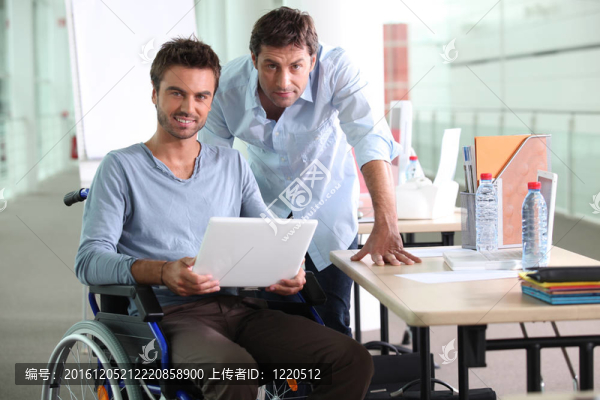 坐在輪椅上的男人在同事旁邊拿著筆記本電腦
