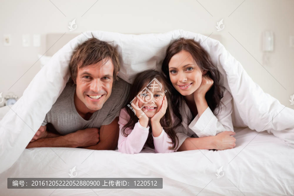 微笑的父母和他們的女兒躺在被窩