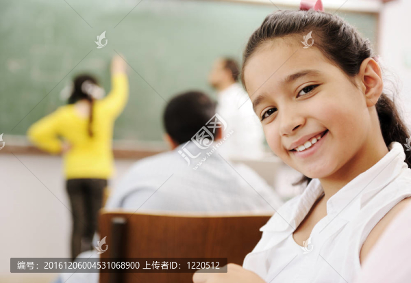 可愛的女孩在學校的教室里微笑，在她的課堂活動后面