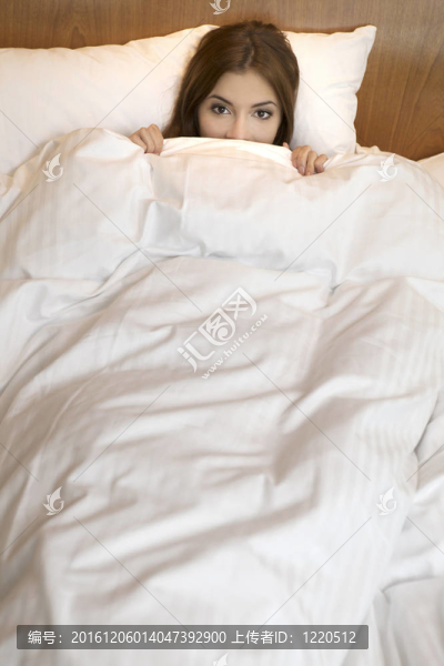 在沉睡的美麗的微笑的女孩白緞子床單下深色的觀點