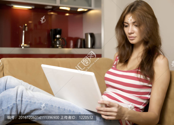 年輕女子躺在白色沙發(fā)上帶筆記本電腦。