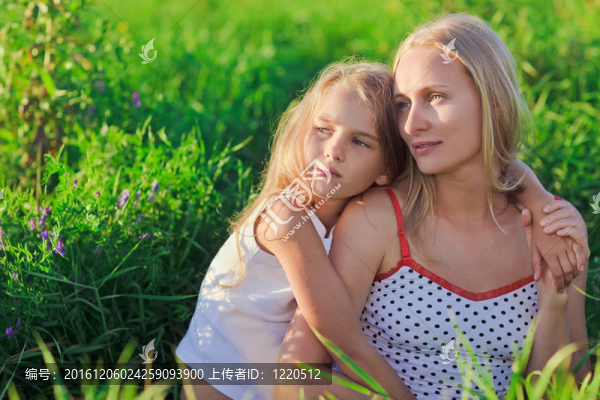 美麗的母女坐在綠色茂盛的草地上，在夕陽(yáng)的陽(yáng)光下