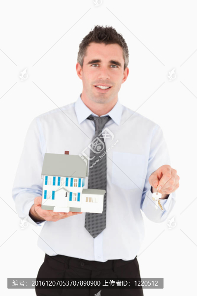 拿著鑰匙和微型房子的男人