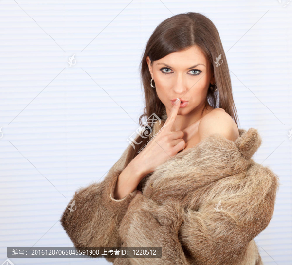 美麗的年輕女子在毛皮大衣手指在嘴里保持沉默