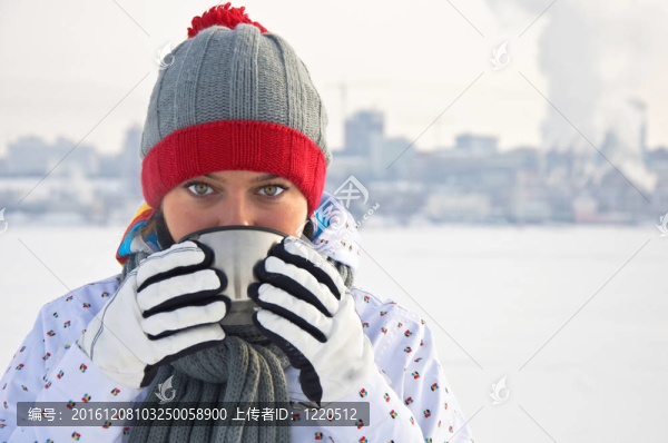 美麗的女人喝熱茶在結(jié)冰的河流的背景下，城市。冬季景觀。