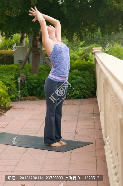 一個運動的棕色頭發(fā)的女人做瑜伽練習拜日式外面人行道上的公眾在一個多云的早晨。