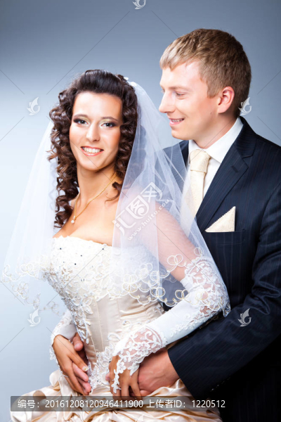 年輕優(yōu)雅的迷戀剛結(jié)婚的新郎望著美麗的新娘，擁抱藍(lán)色背景上的工作室肖像