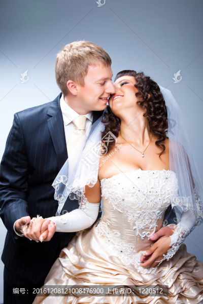 年輕優(yōu)雅的迷戀剛結(jié)婚的新娘和新郎擁抱和親吻藍(lán)色背景上的工作室肖像