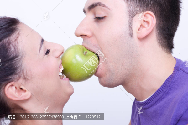 年輕夫婦之間有一個(gè)綠色的蘋(píng)果在他們的嘴唇之間