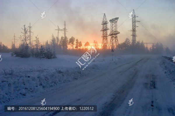 一條冰雪覆蓋的道路環(huán)繞著森林，電線傳送和日落的背景