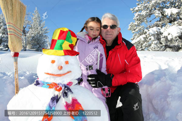 祖父戴著太陽鏡與小孫女在雪人附近滑雪