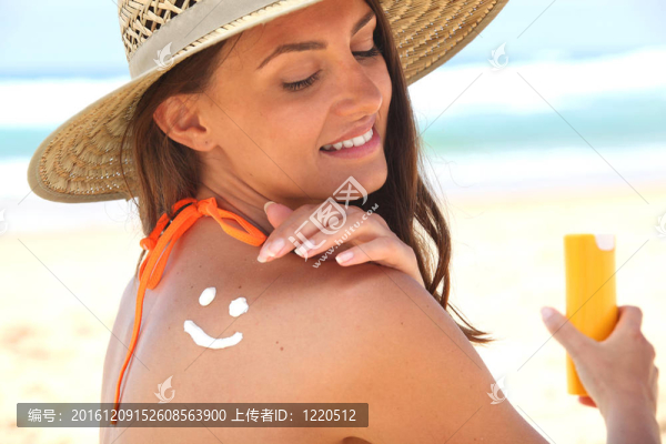 女人坐在沙灘上涂防曬霜