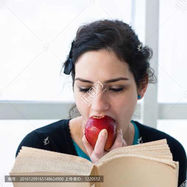 一個漂亮的年輕學(xué)生一邊看書一邊吃蘋果的肖像