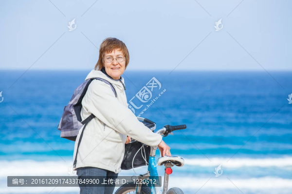 一位漂亮的高級女士騎著自行車在海灘上。