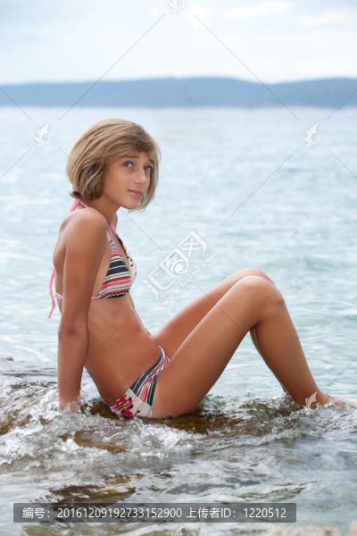 在比基尼坐在海中的巖石上的少女
