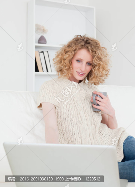 可愛的金發(fā)女人放松她的筆記本電腦坐在她公寓的沙發(fā)上
