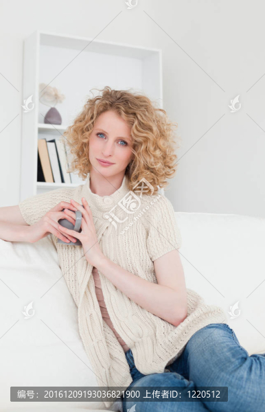 漂亮的金發(fā)女享受一杯咖啡，坐在她公寓的沙發(fā)上