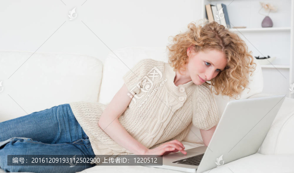 可愛的金發(fā)女人放松她的筆記本躺在她公寓的沙發(fā)上